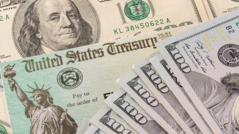 Imagen de un cheque de reembolso de impuestos y de varios billetes de $100 dólares.