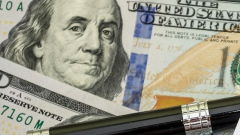 Imagen de una persona que muestra un formulario de impuestos, y se ven una pluma y varios billetes.
