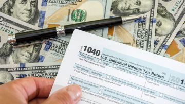 Imagen de una persona que muestra un formulario de impuestos, y se ven una pluma y varios billetes.