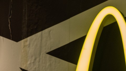 Imagen de una "M" en color amarillo de la marca McDonalds y de una persona que sostiene con las manos un celular.
