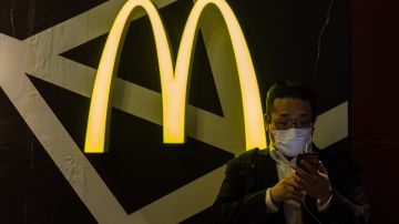 Imagen de una "M" en color amarillo de la marca McDonalds y de una persona que sostiene con las manos un celular.