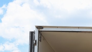 Imagen de un camión con varias cajas y artículos de hogar en la caja, estacionado frente a un conjunto de casas.