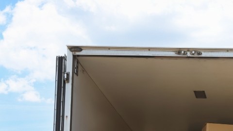Imagen de un camión con varias cajas y artículos de hogar en la caja, estacionado frente a un conjunto de casas.