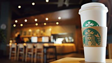Imagen de un vaso de café de Starbucks colocado sobre una barra de madera.