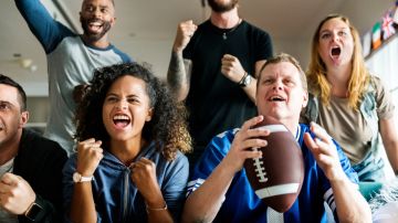 Imagen de varias personas sentadas con gestos de alegría y una sostiene un balón de futbol americano.