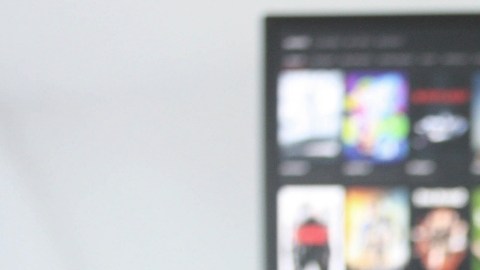 Imagen de una persona que sostiene el control de un televisor con la mano, mientras está frente a una pantalla con opciones de series y películas.