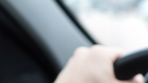 Imagen de una persona que conduce y que muestra un teléfono celular en cuya pantalla se ve el logotipo de la marca Uber.