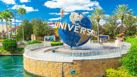 Imagen de un logotipo del parque de diversiones Universal Orlando Resort, en el que se ven árboles y una fuente con agua.