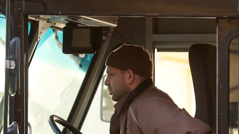 Imagen de una persona que conduce un camión de reparto color café con el logotipo de la marca UPS en un costado.