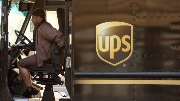 Imagen de una persona que conduce un camión de reparto color café con el logotipo de la marca UPS en un costado.