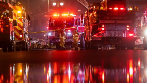 TOPSHOT - Firefighters gather on San Pedro Street after a fire in a single-story commercial building sparked an explosion in the Toy District of downtown Los Angeles on May 16, 2020. - At least 11 firefighters were injured in downtown Los Angeles when a fire in a commercial building sparked a major explosion and spread to nearby structures, fire officials said. Some 230 responders battled the blaze as it spread to other buildings in the area before it was extinguished around two hours after it began. (Photo by Apu GOMES / AFP) (Photo by APU GOMES/AFP via Getty Images)