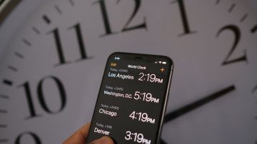 This illustration photo shows a clock in the background of a smartphone showing the time after daylight saving time was implemented in Los Angeles, California, on March 15, 2022. - The US Senate advanced a bill on March 15 that would bring an end to the twice-yearly changing of clocks, in favor of a "new, permanent standard time" that would mean brighter winter evenings. (Photo by Chris DELMAS / AFP) (Photo by CHRIS DELMAS/AFP via Getty Images)