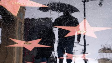 A pedestrian carrying an umbrella is reflected in water along the Hollywood Walk of Fame in Hollywood, California, on January 10, 2023. (Photo by Stefani Reynolds / AFP) (Photo by STEFANI REYNOLDS/AFP via Getty Images)