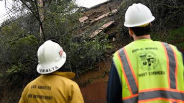 A firefighter and public works crew member look at the damaged hillside from mud flows and a landslide below a home above Mulholland Drive following heavy rain from winter storms on February 28, 2023 in Los Angeles, California. (Photo by Patrick T. Fallon / AFP) (Photo by PATRICK T. FALLON/AFP via Getty Images)