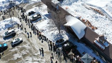 CRESTLINE, CALIFORNIA - MARCH 03: An aerial view of residents (L) waiting in line to receive donated food outside the local grocery store (R), which was severely damaged when its roof collapsed under the weight of several feet of snow, after a series of winter storms in the San Bernardino Mountains in Southern California on March 3, 2023 in Crestline, California. Some residents have been stranded in Crestline more than a week due to heavy snowfall while the grocery store was the main hub for food purchases in town. California Governor Gavin Newsom has declared a state of emergency due to winter storms for 13 counties including San Bernardino County and the California National Guard is assisting relief efforts in the mountains. (Photo by Mario Tama/Getty Images)