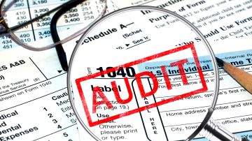 Imagen de formularios de impuestos, una lupa y un sello de color rojo con la palabra auditoría en inglés.