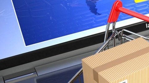 Imagen de un carrito de supermercado en miniatura, con unas cajas en miniatura, sobre el teclado de una computadora portátil y dos tarjetas de crédito.