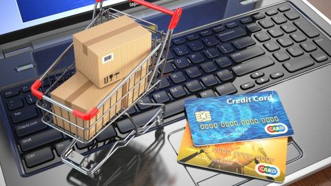 Imagen de un carrito de supermercado en miniatura, con unas cajas en miniatura, sobre el teclado de una computadora portátil y dos tarjetas de crédito.
