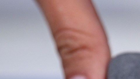 Imagen de un diamante de color rosa que está montado en un anillo de color plata, sujeto a una caja de color gris, que es sostenida por tres dedos.