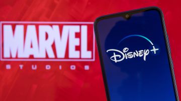 Imagen de un fondo de color rojo con las letras de la marca Marvel y de un teléfono celular en cuya pantalla se ve el logotipo de la empresa Disney+.