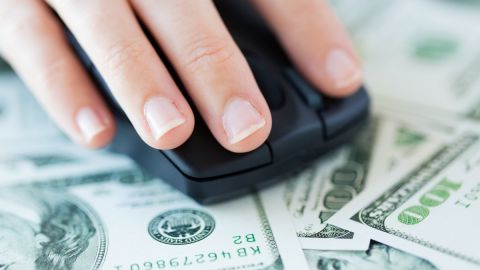 Imagen de una mano sobre un mouse, que está sobre varios billetes.