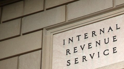 Imagen de un edificio del IRS, con una placa que muestra la leyenda Internal Revenue Service, en medio de un semáforo en color verde.