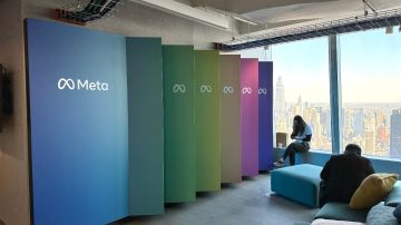 Imagen de una oficina con mamparas de varios colores que tienen el logotipo de la empresa Meta. También se ven a dos personas sentadas.