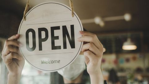 Imagen de una persona que está colocando un letrero de "abierto" en inglés "open" en un aparador.