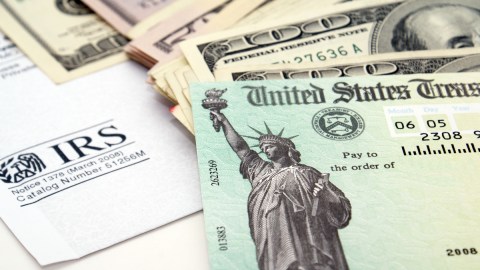 Imagen de un cheque de reembolso de impuestos, junto con varios billetes y un formulario del IRS.