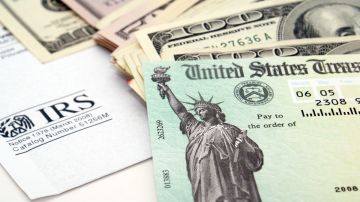 Imagen de un cheque de reembolso de impuestos, junto con varios billetes y un formulario del IRS.