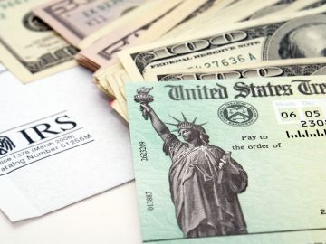 Imagen de un cheque de reembolso de impuestos, junto con varios billetes y un formulario del IRS.