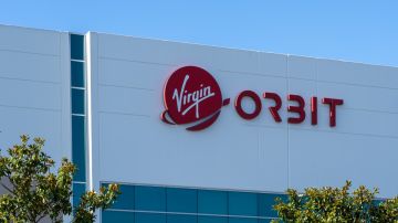 Imagen de un edificio con muros blancos en los que se ve el logotipo de la empresa Virgin Orbit en color rojo.