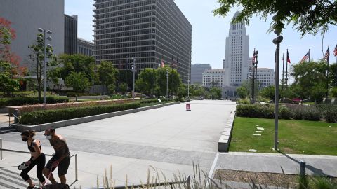 A man and woman wearing facemasks walk dogs in Grand Park with Los Angeles City Hall seen in the background, June 24, 2020 in Los Angeles, California during the coronavirus pandemic. - For the second consecutive day, California shattered daily records for new COVID-19 cases, yesterday with more than 6,600 infections reported, the largest single-day count in California since the pandemic hit. US Rep.Adam Schiff (D-Burbank) today introduced legislation to provide free cloth face coverings via United States mail to any American who requests one, as well as authorize further research into mask efficacy to reduce the spread of COVID-19, as many Americans continue to resist the call to wear face coverings in public. (Photo by Robyn Beck / AFP) (Photo by ROBYN BECK/AFP via Getty Images)