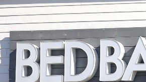 Imagen del acceso de una tienda de la cadena Bed Bath & Beyond, con una persona que camina hacia la entrada.