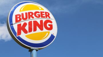 Imagen de un letrero de la marca Burger King, en colores azul, amarillo, rojo y blanco, en medio del cielo azul.