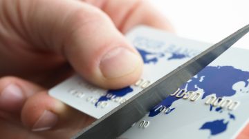 Imagen de unas manos que cortan una tarjeta de crédito con unas tijeras.