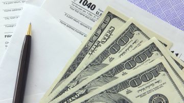 Imagen de varios billetes sobre un sobre postal, una pluma y un formulario de impuestos.