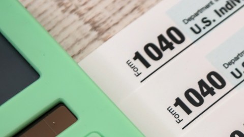 Imagen de varios formularios de impuestos, junto con una pluma y una calculadora de color verde.
