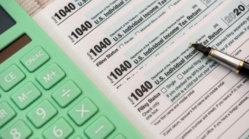 Imagen de varios formularios de impuestos, junto con una pluma y una calculadora de color verde.