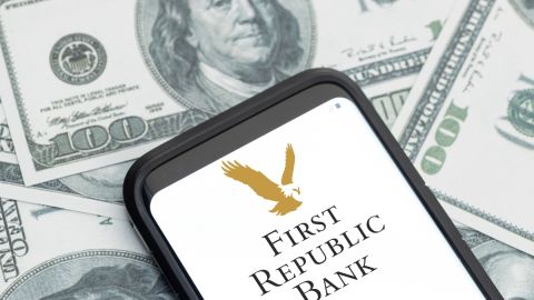 Imagen de un teléfono celular en cuya pantalla se ve el logotipo de First Republic Bank, y de varios billetes de $100 dólares.