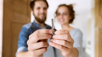 Imagen de dos personas en un segundo plano que sostienen la llave de una vivienda en las manos.