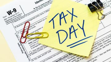 Imagen de un post-it de color amarillo con la frase Tax Day en color azul, sobre un formulario de impuestos y unos clips.