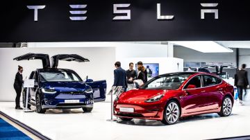 Imagen de dos vehículos de Tesla, uno en color azul y otro en rojo, en medio de una sala de exhibiciones.