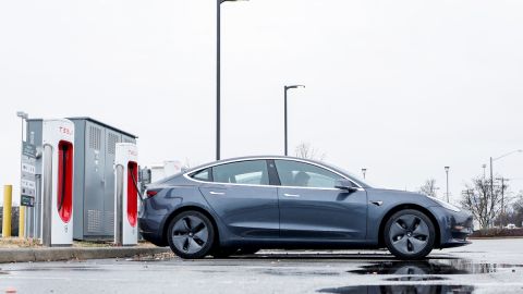 Imagen de una estación de carga para vehículos eléctricos y de un automóvil de la marca Tesla, de color gris.