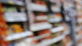 Imagen de una persona que empuja un carrito de compra en medio del pasillo de un supermercado.