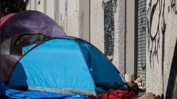 A homeless person lies in their tent on the sidewalk in front of the non-profit Midnight Mission's headquarters, while traditional Thanksgiving meals are served to nearly 2000 homeless people in the Skid Row neighborhood of downtown Los Angeles on November 25, 2021. (Photo by Apu GOMES / AFP) (Photo by APU GOMES/AFP via Getty Images)