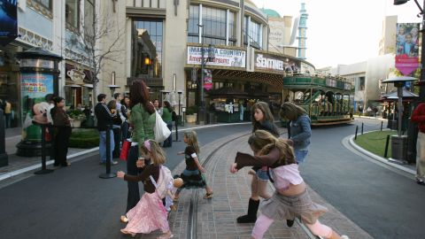 Los Angeles, UNITED STATES: 3/4 TO GO WITH AFP STORY: US-SOCIETY-DISTRIBUTION-REAL ESTATE Shoppers cross a street lined at The Grove outdoor shopping mall, 24 April, 2006, in Los Angeles. The Grove was inaugurated in 2002 and spreads out over more than 15 acres (five hectares). Its owner, the promoter Rick Caruso, claims that 18 million people visit the mall a year, more than Disneyland. AFP PHOTO / Robyn BECK (Photo credit should read ROBYN BECK/AFP via Getty Images)