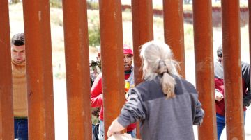 Un hombre habla con padres de familias que se quedaron al otro lado de la valla fronteriza en San Diego.