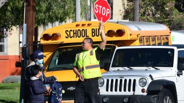 (FILES) In this file photo a woman wears a facemask picking up a child as an Alhambra Unified School District as a crossing guard stops traffic outside Ramona Elementary School on February 4, 2020 in Alhambra, California. - As the coronavirus pandemic forces the closing of more schools and workplaces, the health crisis has exposed the "digital divide" which allows some to stay on task remotely, with others left out.A growing number of students from grade school to university are moving to virtual classrooms, and while millions of office workers are being asked to work from home as a result of the expanding public health emergency. (Photo by Frederic J. BROWN / AFP) (Photo by FREDERIC J. BROWN/AFP via Getty Images)