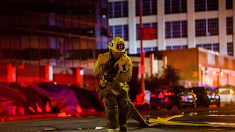 A firefighter drags a hose on San Pedro Street after a fire in a single-story commercial building sparked an explosion in the Toy District of downtown Los Angeles on May 16, 2020. - At least 11 firefighters were injured in downtown Los Angeles when a fire in a commercial building sparked a major explosion and spread to nearby structures, fire officials said. Some 230 responders battled the blaze as it spread to other buildings in the area before it was extinguished around two hours after it began. (Photo by Apu GOMES / AFP) (Photo by APU GOMES/AFP via Getty Images)